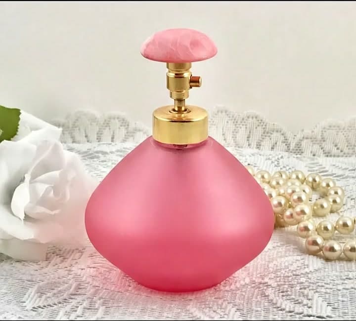 Product photo of a pink perfume bottle on white lace with pearls